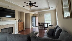 Ein Wohnzimmer mit grauem Sofa, Kamin, Flachbildfernseher und Deckenventilator.
