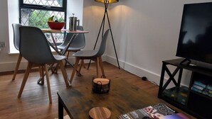 A modern living room with a wooden coffee table, a floor lamp, a television, and a dining area with chairs and a table.