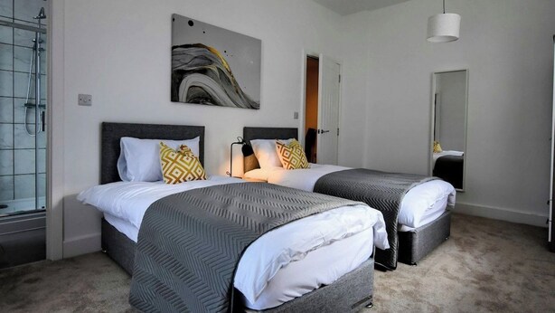 A hotel room with two beds, a shower, a painting on the wall, and a door.
