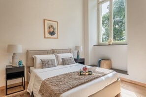 Un dormitorio con una cama, dos mesitas de noche, una ventana y un cuadro enmarcado en la pared.