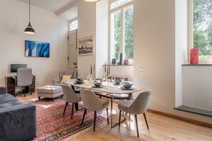 Un comedor con una mesa dispuesta para cuatro personas, un sofá gris, un tapete con estampado rojo y un cuadro en la pared.