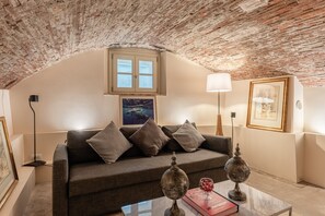 Een gezellige woonkamer met een bakstenen plafond, een bank met kussens, een tafel met decoratieve objecten en lijstwerken aan de wanden.