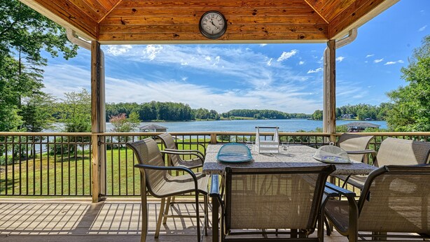 A covered outdoor area with a table and chairs, overlooking a lake and forest.