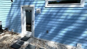 A house with blue siding, a white door labeled 'HAPPY PLACE,' a small window, and a gravel pathway leading to the door.