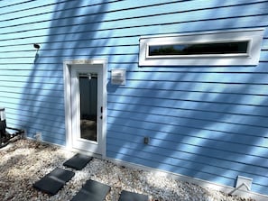 Une maison avec un revêtement bleu, une porte blanche sur laquelle on peut lire «ENDROIT HEUREUX», une petite fenêtre et un chemin de gravier menant à la porte.