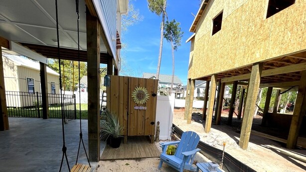 A covered outdoor area with a swing set, Adirondack chairs, and a wooden deck.