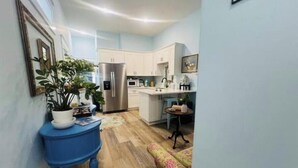 A compact kitchen with white cabinets, a stainless steel refrigerator, and a small dining area with a floral sofa.