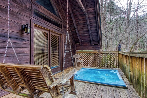 Una terraza de madera con un jacuzzi, una hamaca y vistas a un bosque.