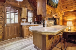 A wooden cabin interior with a kitchen island, wooden cabinets, and a window with blinds.