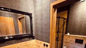 Un baño moderno con tocador de madera, lavamanos de piedra, un espejo grande y cabina de ducha con paredes de vidrio.
