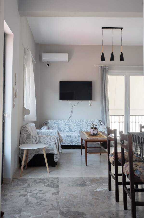 A modern living room with a sofa, a dining table, and a TV mounted on the wall.