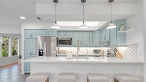 A modern kitchen with light blue cabinets, a large island with bar stools, stainless steel appliances, and pendant lighting.