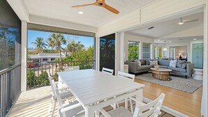 A spacious balcony with a dining area, a living room with a sofa and coffee table, and a view of palm trees and a white building.