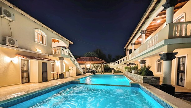 A swimming pool with a stone border, surrounded by buildings with balconies and columns.