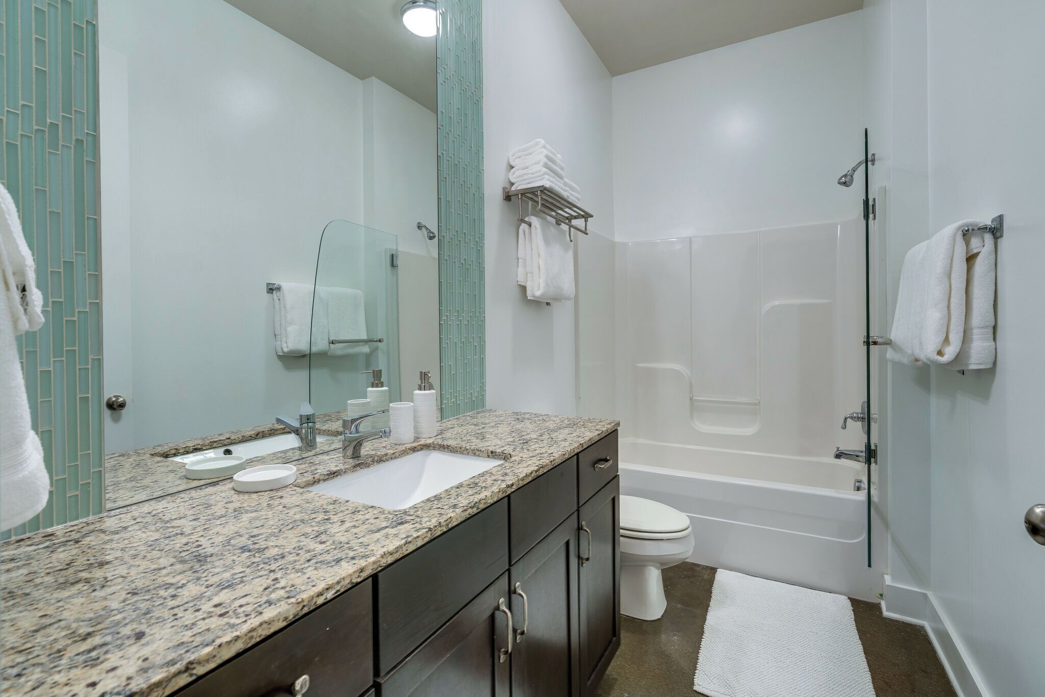 A modern bathroom with a granite countertop sink, a toilet, a bathtub, and a glass shower enclosure.