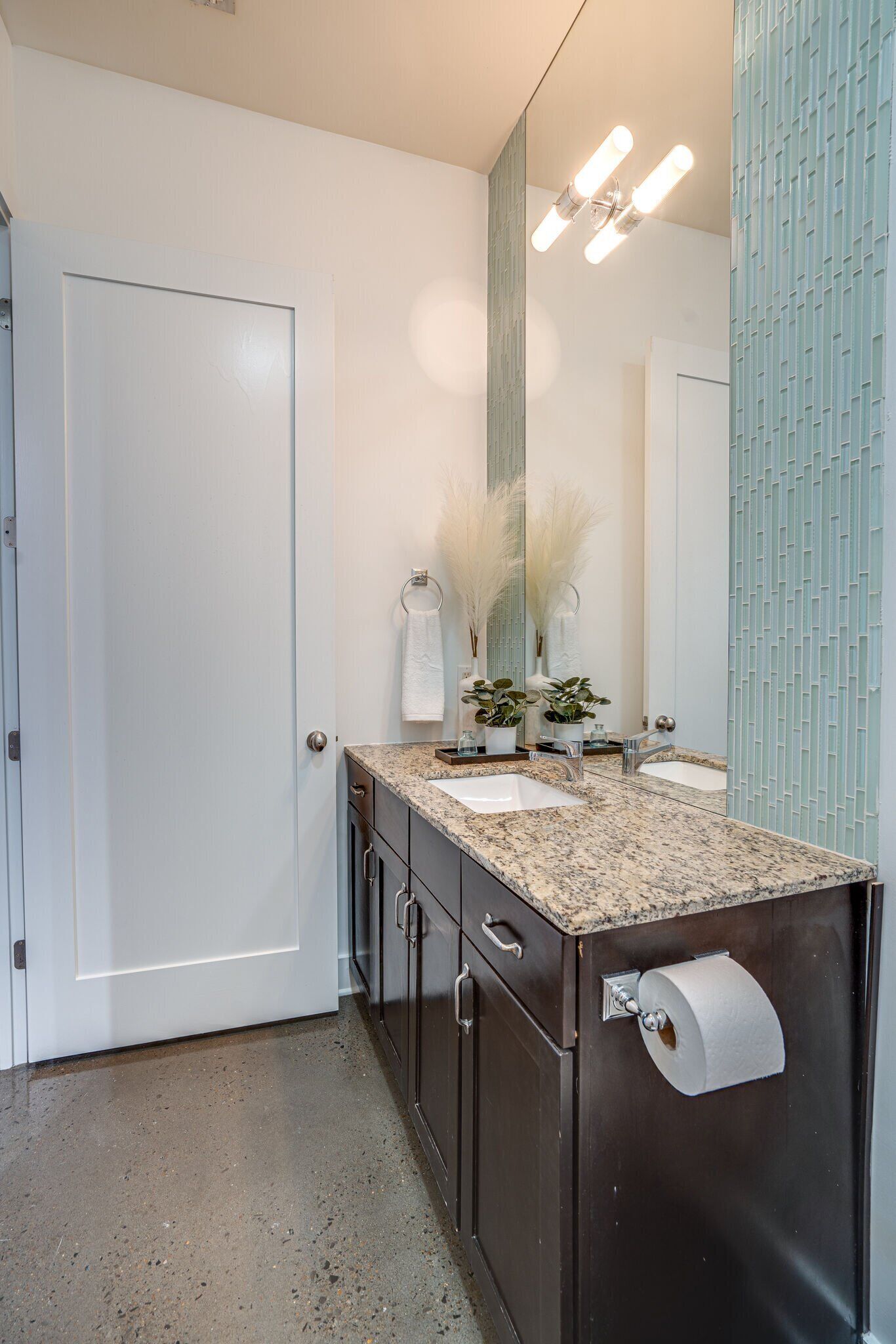 A bathroom with a marble countertop, two sinks, a large mirror, and a towel rack.