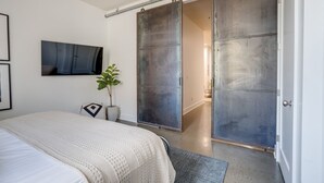 Un dormitorio con cama, puerta corredera, planta en maceta y televisor montado en la pared.