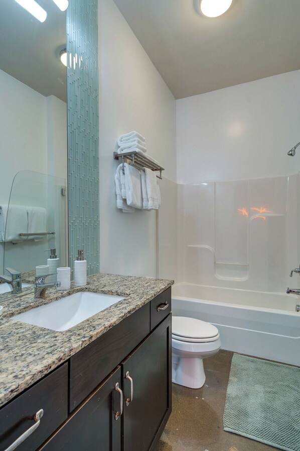 A modern bathroom with a granite countertop, a white sink, a toilet, and a glass-enclosed shower. - Lofts At 30th - Urban Lodge - Mins to Broadway! (Nashville)