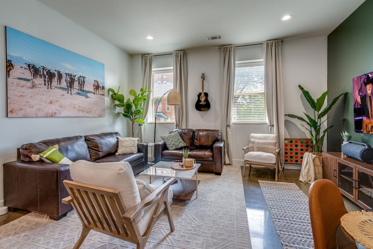 Een moderne woonkamer met een groot schilderij, een gitaar en diverse zithoeken.