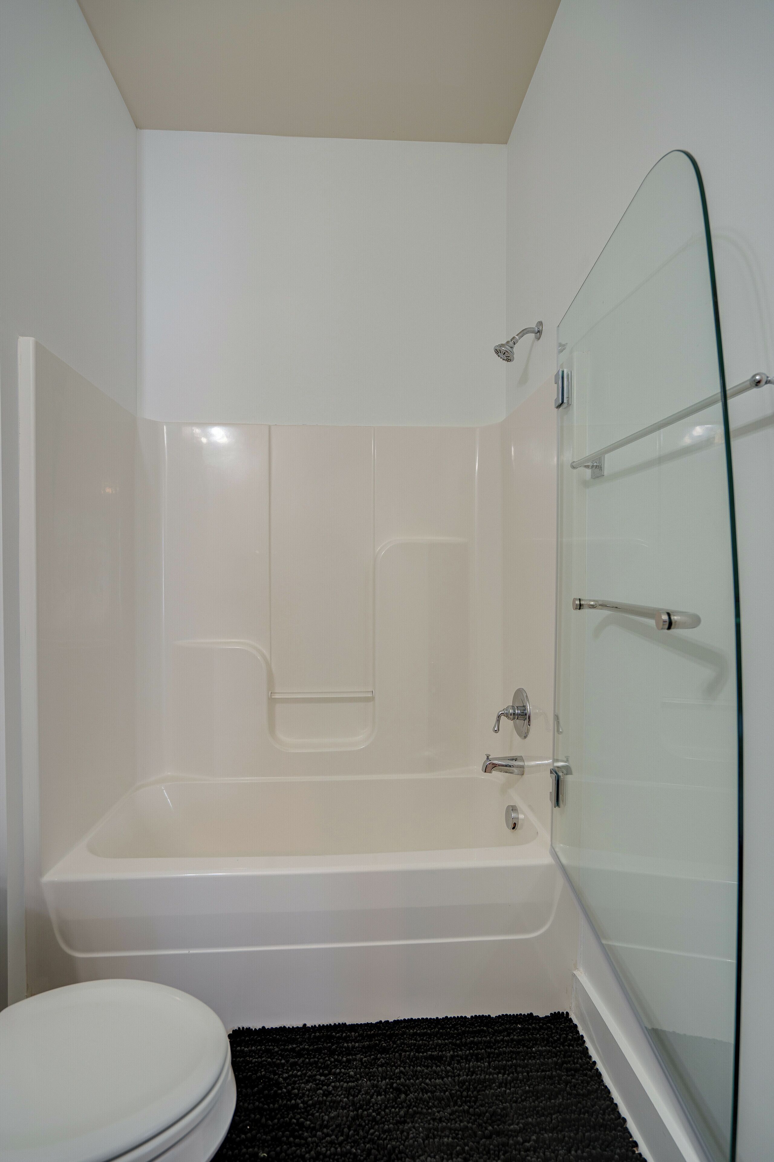 A modern bathroom with a glass shower enclosure, a white bathtub, and a black bath mat.