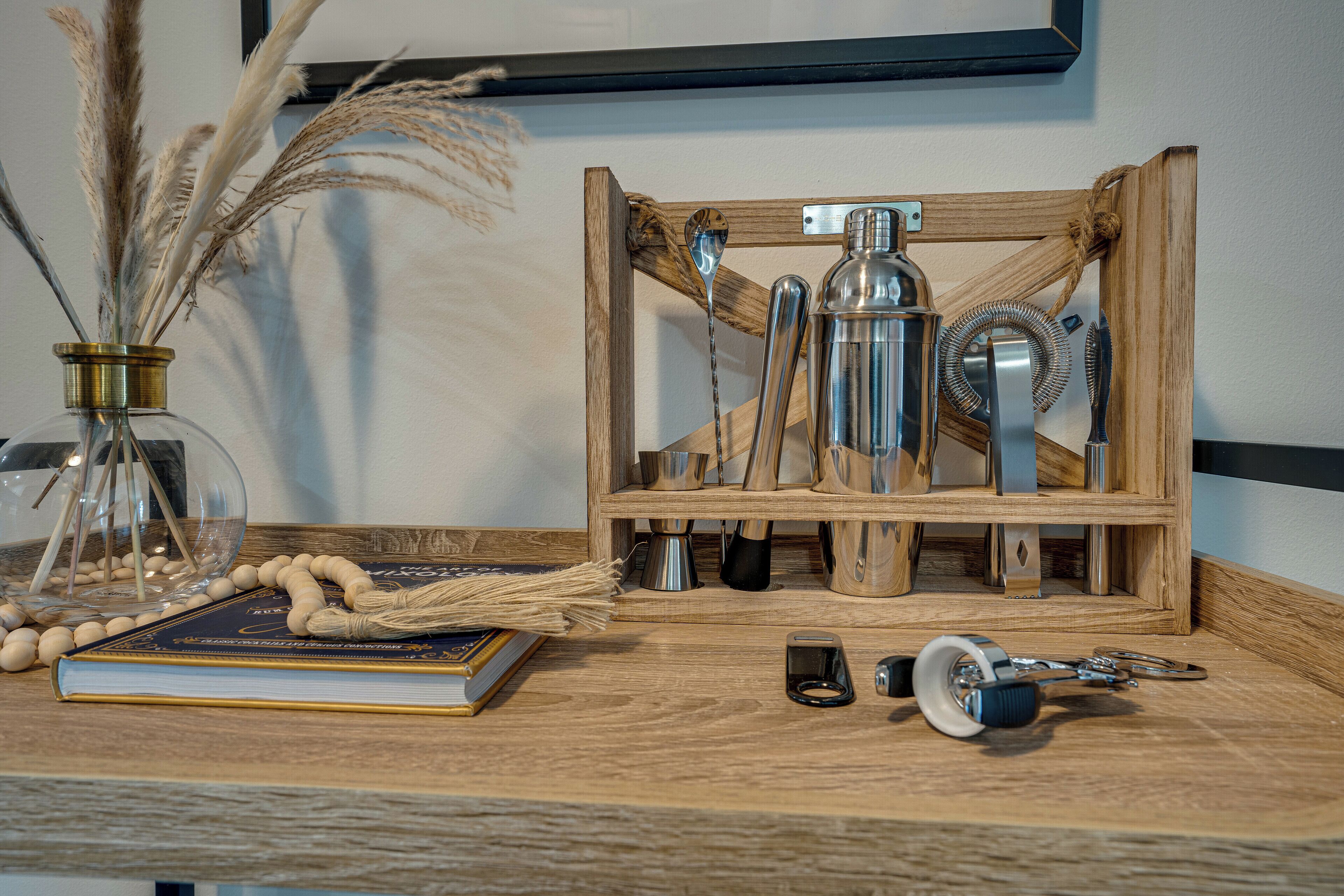 Una mesa de madera con un libro, un florero de vidrio con plantas secas y una botella de metal.