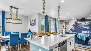 A modern kitchen with a central island, blue chairs, and a dining area. - Entertainment Oasis 4BR w/ Home Theater & Game Room (Commerce City)