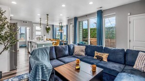 A modern living room with a sectional sofa, a wooden coffee table, and a view of the kitchen and outdoor area. - Entertainment Oasis 4BR w/ Home Theater & Game Room (Commerce City)