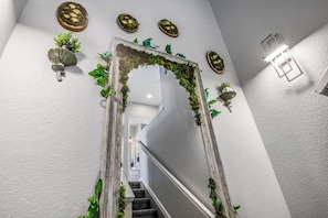 A staircase with a wooden frame and greenery, white walls, and decorative wall sconces.