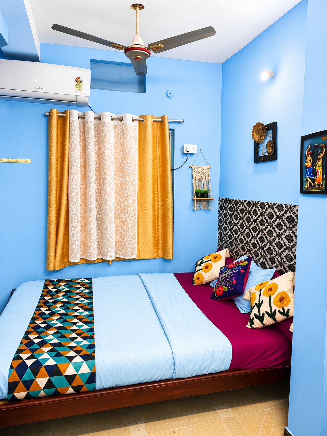 A room with a bed, a ceiling fan, an air conditioning unit, a wall-mounted light, and a framed picture.