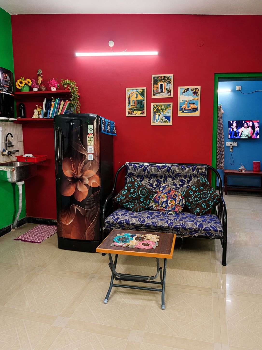 Una sala de estar con un sofá, una mesa de centro, un refrigerador, un televisor y obras de arte en la pared.