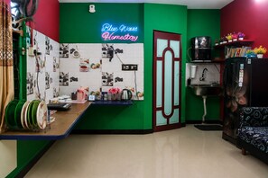 A room with a green accent wall, a neon sign, a kitchen area with a sink, and a black sofa.
