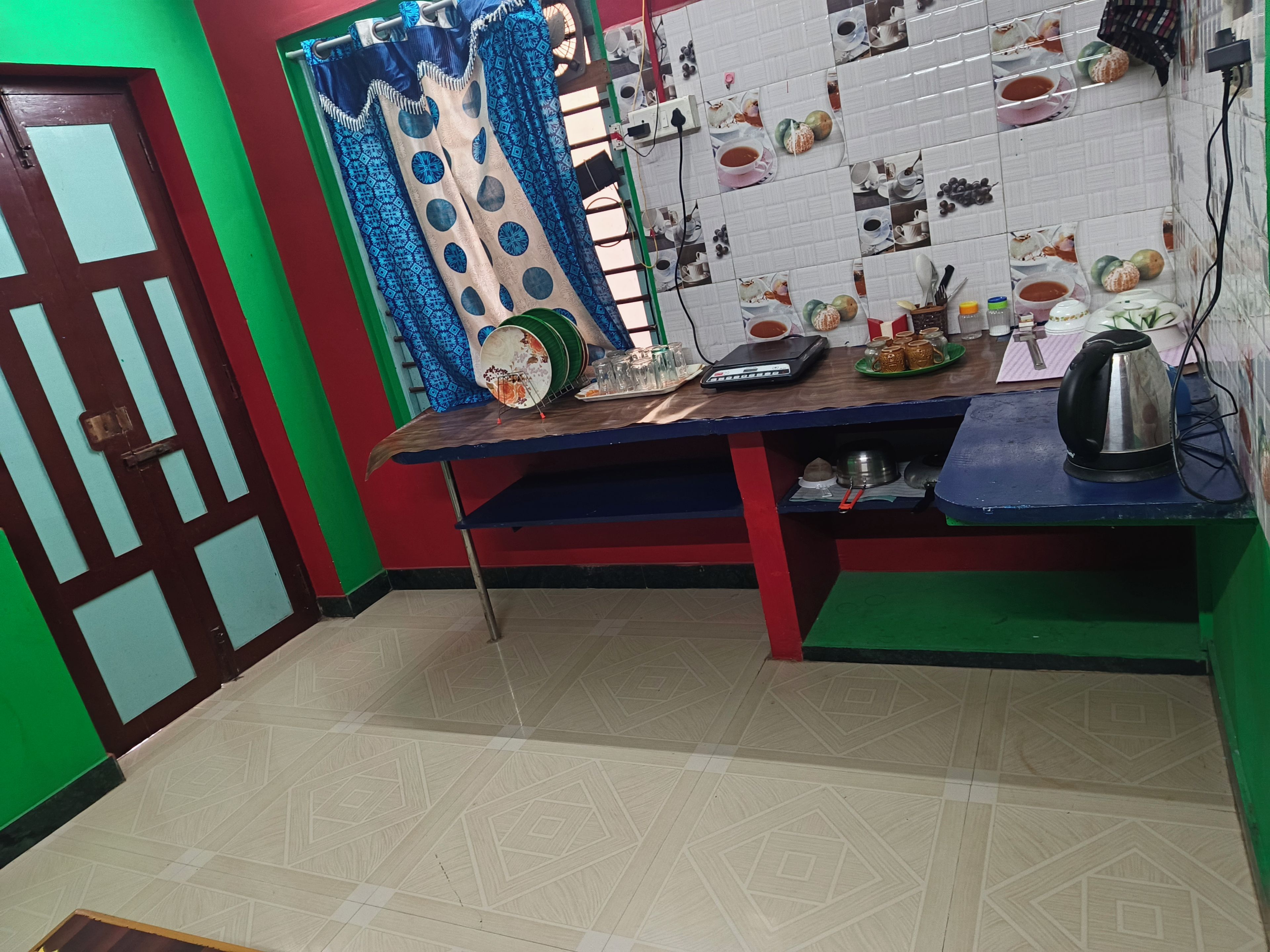Una cocina con salpicadero de azulejos, una mesa con diversos utensilios de cocina y una puerta con diseño geométrico.
