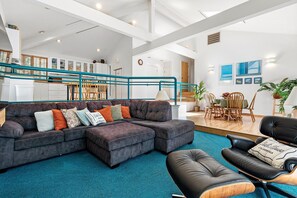 Un salon moderne avec un canapé d’angle, un fauteuil en cuir noir et un coin repas comprenant des chaises et une table en bois.