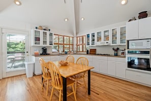 Une cuisine moderne avec des meubles blancs, une table à manger en bois et une vue par la fenêtre.