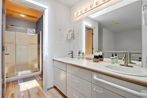 Une salle de bain avec une douche en verre, deux lavabos, un grand miroir et un porte-serviettes.