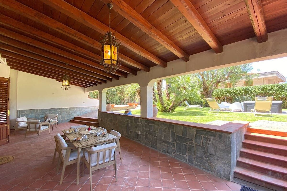 An outdoor patio with a stone wall, wooden ceiling, and a table set for dining.