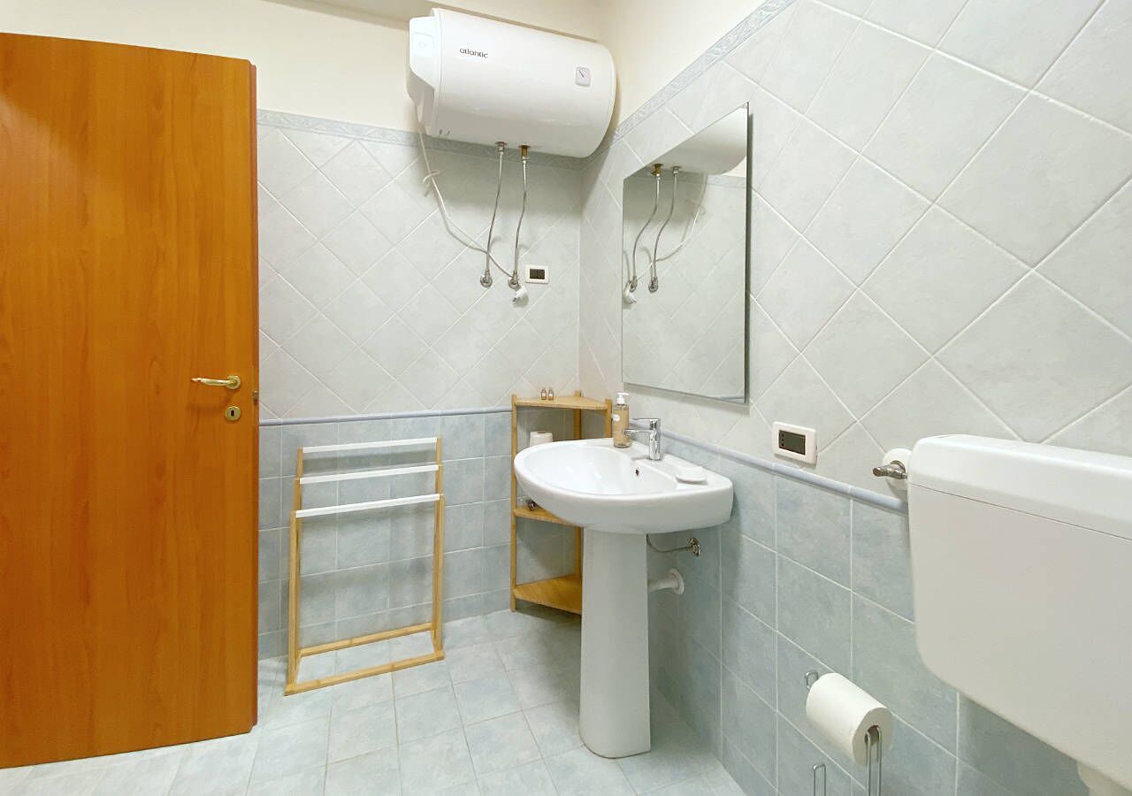 Une salle de bain avec une porte en bois, un lavabo blanc, un miroir et des toilettes.
