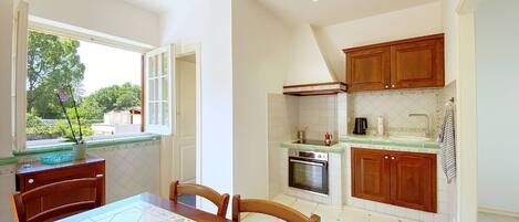 A compact kitchen with wooden cabinets, a built-in oven, and a window with a view of greenery.