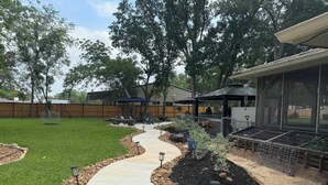 A backyard with a curved pathway, a grill area, and a covered seating space.