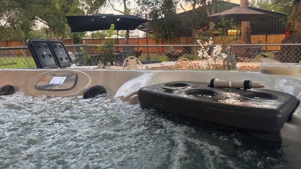A hot tub with a control panel, surrounded by a wooden deck, chairs, and a fence.