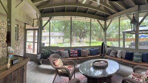 A covered outdoor seating area with a pool table, a round table, and a stone fireplace.