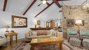 A spacious living room with a high ceiling, exposed beams, a large wooden coffee table, and a stone accent wall.