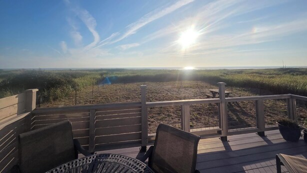 A deck with chairs overlooking a beach with a clear sky and the sun setting or rising.