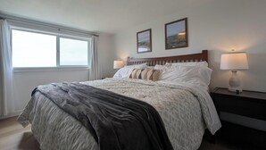 A neatly made bed with a grey blanket, white pillows, and a patterned duvet. There are two wall-mounted lamps on either side of the bed.
