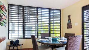 A dining area with a round table, wicker chairs, and a window with blinds.