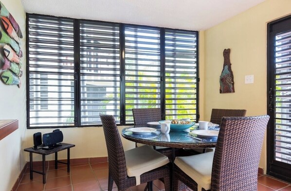 A dining area with a round table, wicker chairs, and a window with blinds.
