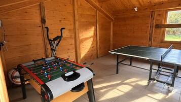 Una habitación con mesa de fútbolín, mesa de ping pong y ventana que deja entrar luz natural.