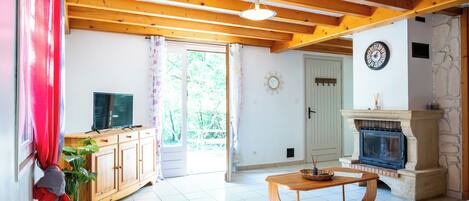 Una sala de estar con chimenea, vigas de madera en el techo, televisor y ventana con cortinas.