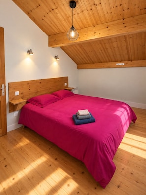 Un dormitorio con techo de madera, una cama con colcha roja y dos lámparas de pared.