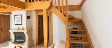 Una escalera de madera que lleva a un nivel superior, una chimenea y una cama con colcha estampada.